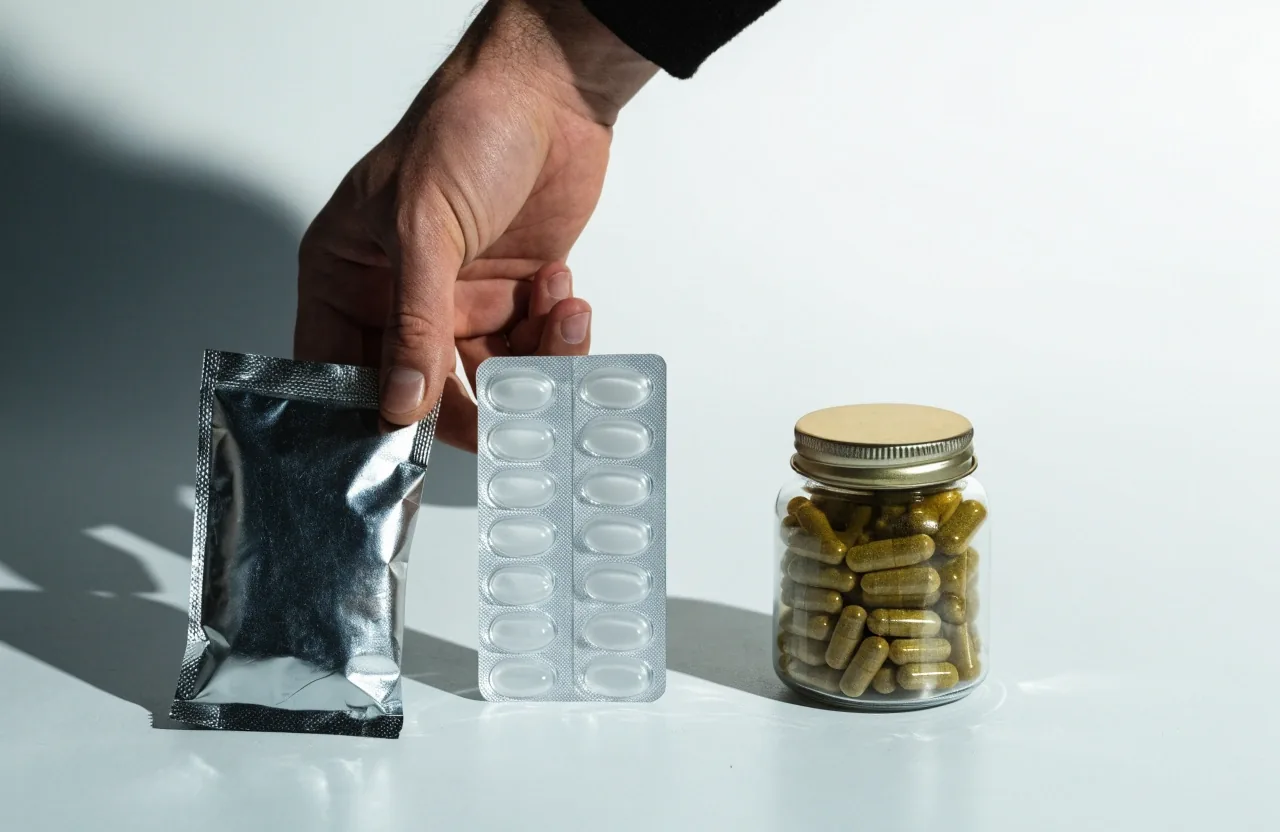Trois formats posés sur un fond clair: un sachet, une plaquette alvéolée non imprimée et un petit flacon de gélules, ombre nette à droite.